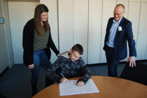 Lehrerin Christina Walder (l.) und der Schulleiter der Heinrich-Böll-Schule, Alexander Hauptmann (r.) beglückwünschen Schüler Leland zum Erfolg.