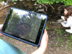 Das Bild zeigt die Schüler/innen bei den Temperatur-Messungen am Bach mit Messelektrode und iPad