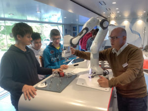 Das Bild zeigt Schülerinnen und Schüler mit einem Mitarbeiter und einem Roboterarm.