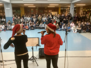 Lehrkräfte und Schüler singen und musizieren im Foyer der Schule mit vielen Schüler/innen als Zuschauer