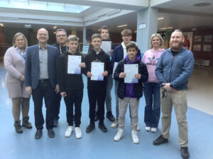 Schulleiter und Mathelehrer stehen mit den Siegern des Mathewettbewerbs im Foyer der Schule