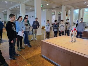 Schüler stehen im Halbkreis um Roboter auf Tisch