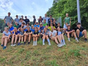 Schüler/innen sitzen auf der Wiese. Dahinter stehen zwei Lehrkräfte