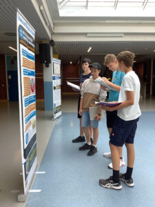 Vier Schüler stehen vor einem Plakat-Aufsteller und lesen die Inhalte