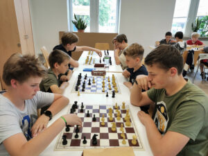 Das Bild zeigt Schüler, die sich an einem langen Tisch gegenübersitzen und jeweils zu zweit Schach gegeneinander spielen