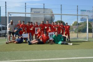 Die Sieger der HBS Fußballmannschaft posieren zusammen im Tor auf dem Fußballplatz