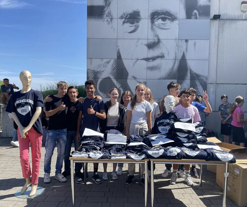 Schüler/innen stehen am Verkaufsstand der neuen Schulshirts und Pullis