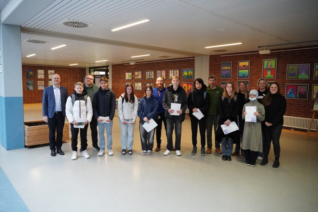 Die Schülerinnen und Schüler stehen im Foyer zeigen ihre Urkunden, die sie gerade von Fachsprecherin Claudia Fellenberg (im Bild rechts hinten) und im Beisein des Schulleiters Alexander Hauptmann (im Bild links) erhalten haben