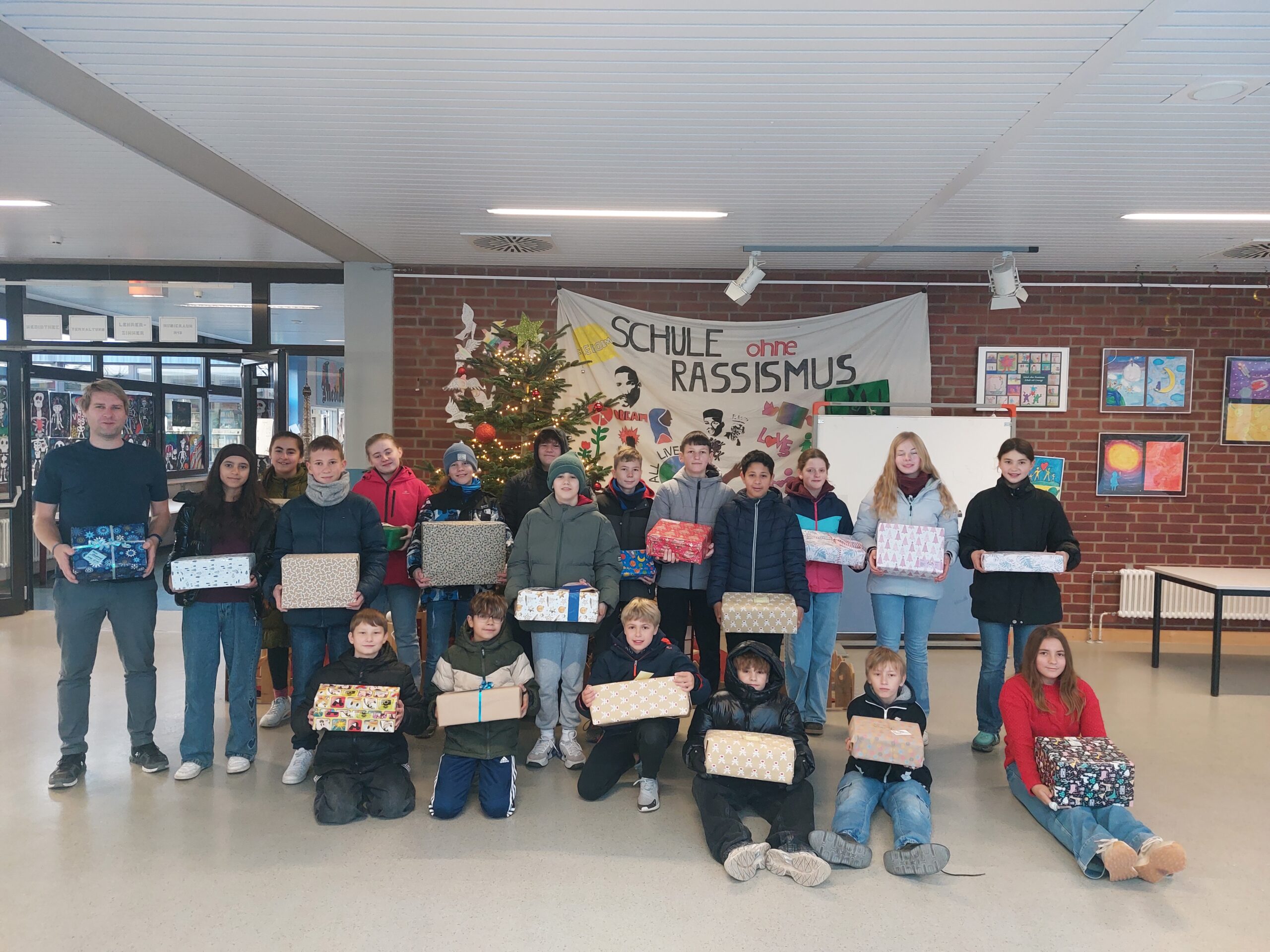 Lehrer Markkus Hantke und seine Klasse befinden sich vor dem Weihnachtsbaum Foyer und halten Päckchen in der Hand