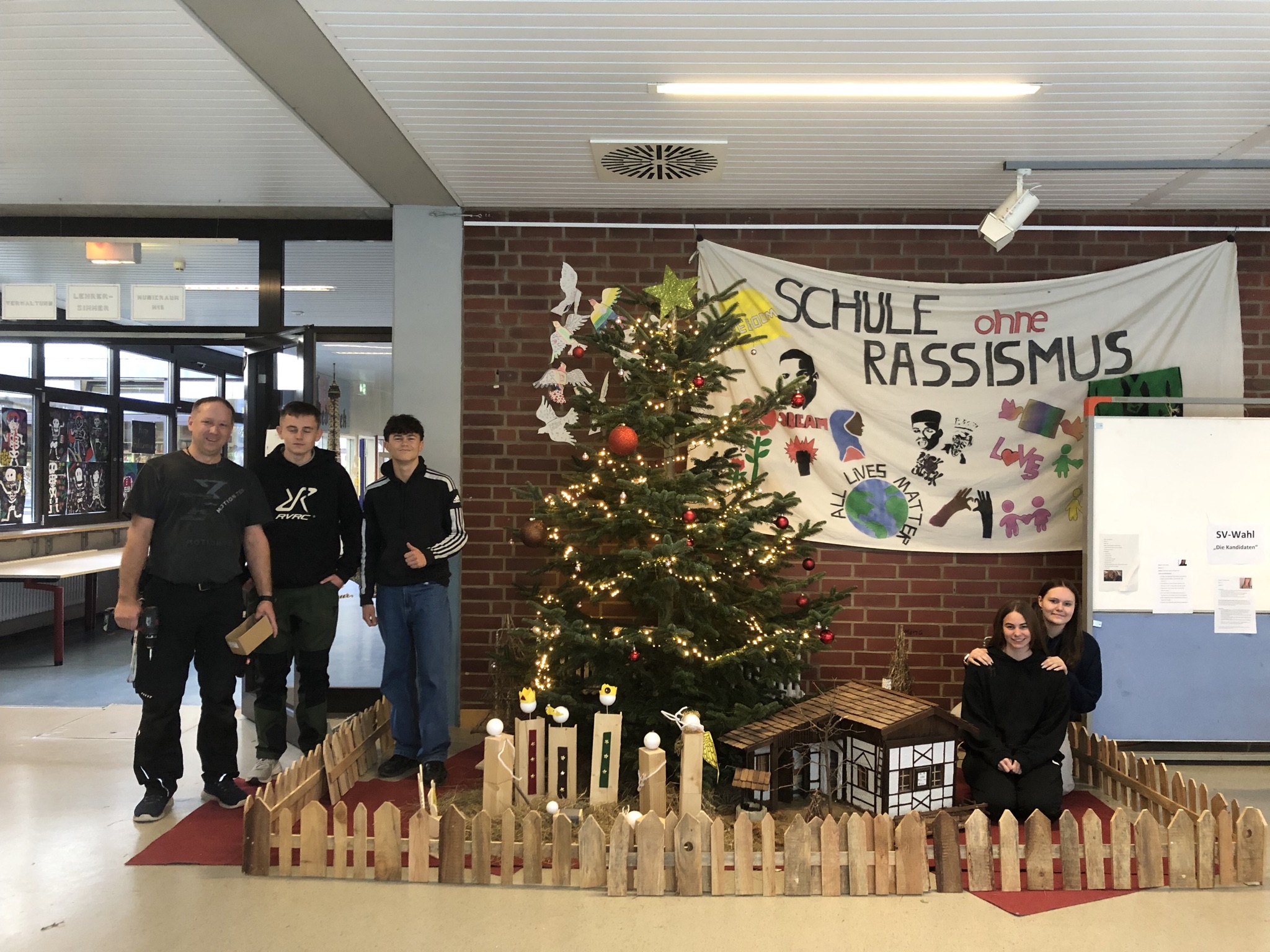 Der geschmückte Weihnachtsbaum im Foyer der Schule und darum die Schüler/innen und Hausmeister, die ihn geschmückt haben