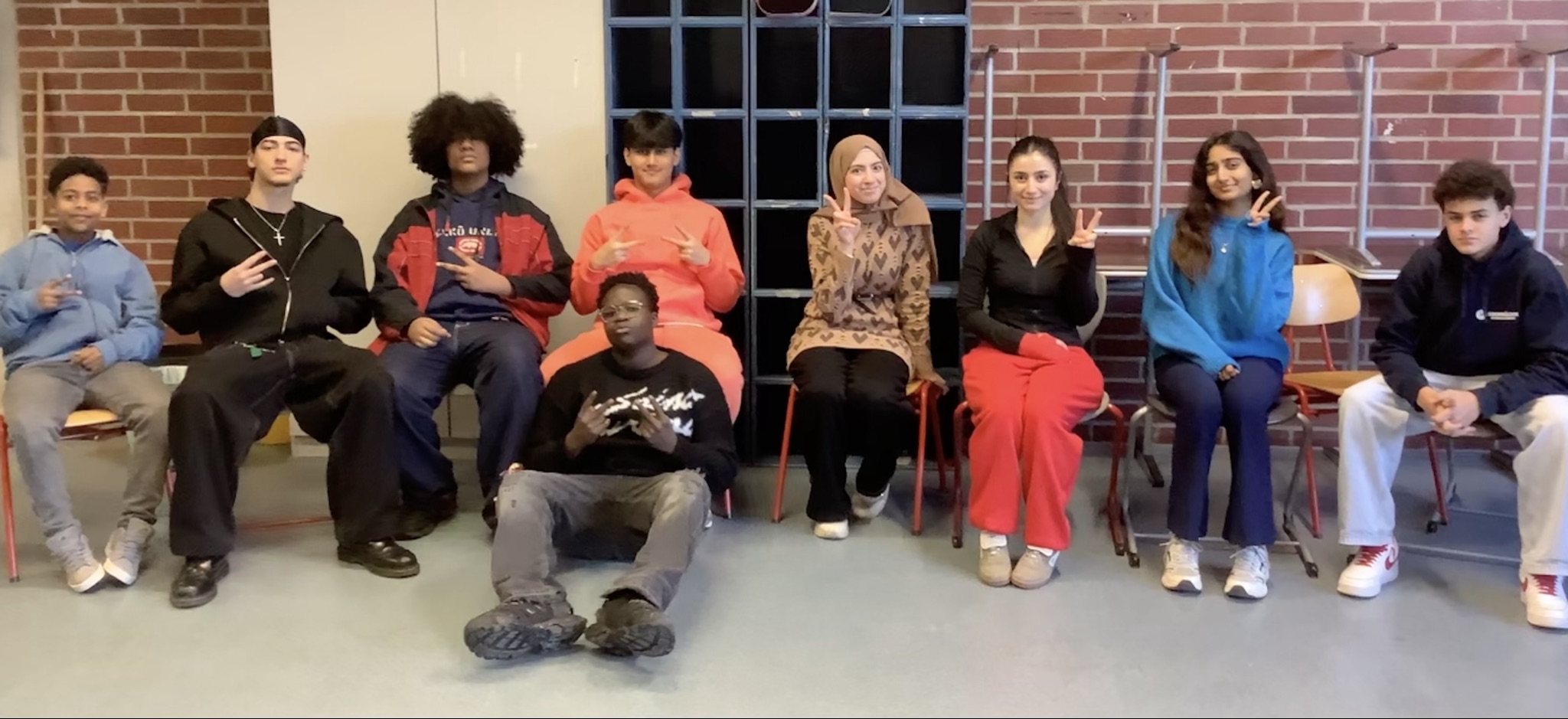 Die Schüler/innen Ashkan Abdulahi, Samuel Eckert, Gazy Hassan, Malik Igbinedion, Fisia Ali Minawr, Fabio Minella, Srinika Sujith, Sedra Al Naasan, Yafet Araya sitzen in einer Reihe auf Stühlen