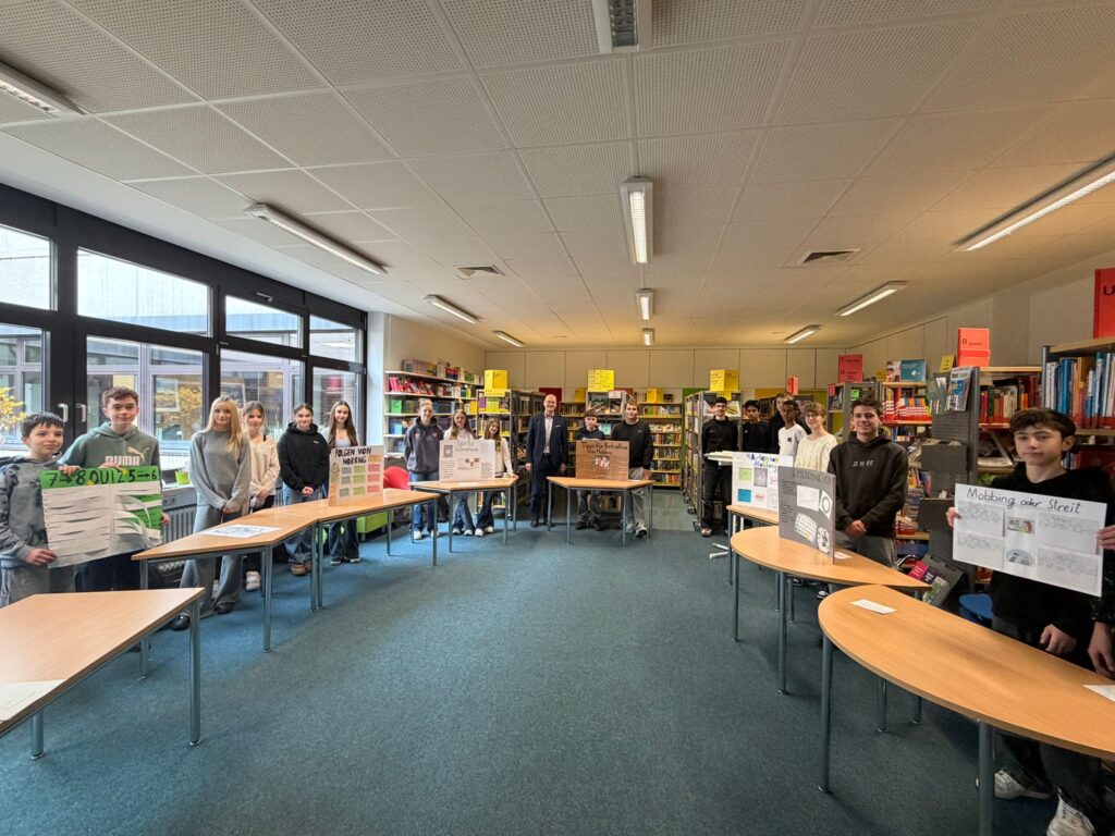 Schüler/innen zeigen Plakate zu einem Deutsch-Projekt in der Mensa im Halbkreis
